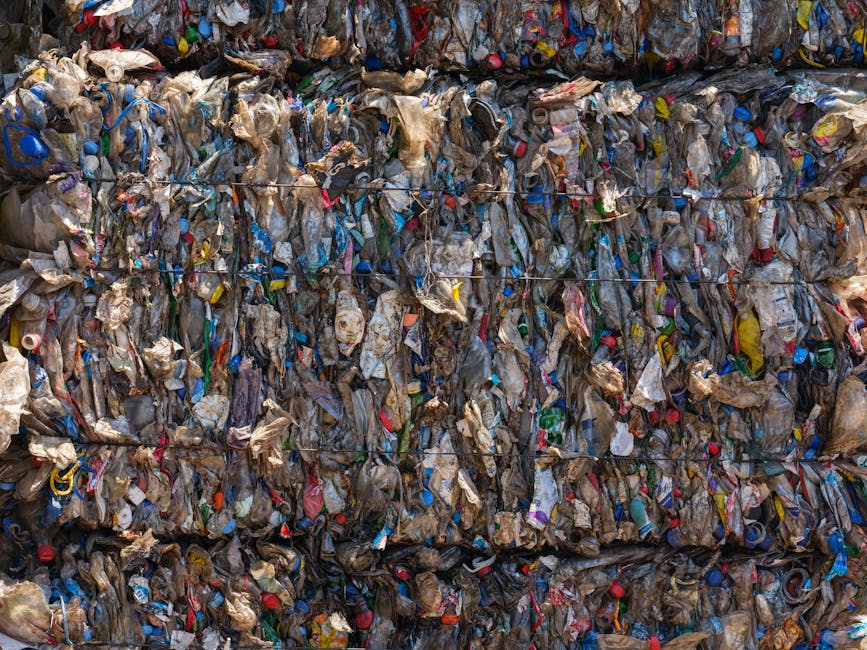 A large, tightly compressed boulder of mixed waste materials featuring various colors and textures, primarily consisting of crumpled and torn plastic and paper debris. The waste is secured with multip